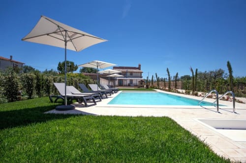 Casale 905 pool area in Crecchio with loungers, umbrellas, and rustic villa in clear sunny day