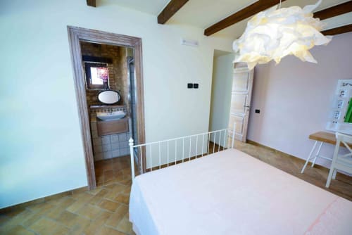 Bright bedroom at Casale 905 B&B in Crecchio with white metal bed, exposed beams, bathroom, and modern pendant light