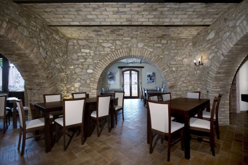 Rustic stone dining room at Casale 905 B&B in Crecchio with wooden tables, white chairs, and arched brick ceiling