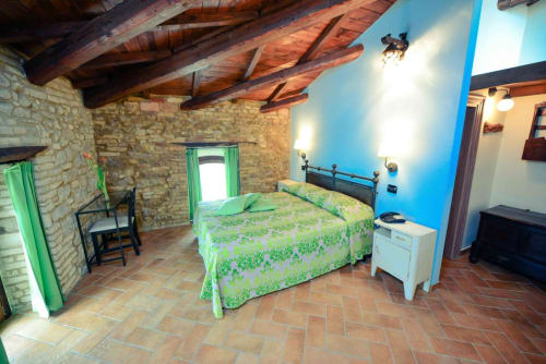 Rustic bedroom at Casale 905 B&B in Crecchio with exposed beams, terracotta floors, green bedding, and stone walls.