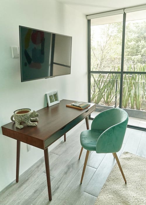 Espacio de trabajo moderno en hotel de CDMX con escritorio de madera, silla de terciopelo verde, TV de pared y ventanales del piso al techo con vistas