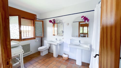 Spacious bathroom at Casa Rural Villa del Jerte with dual sinks, pedestal basin, wooden frames and terra cotta tiles