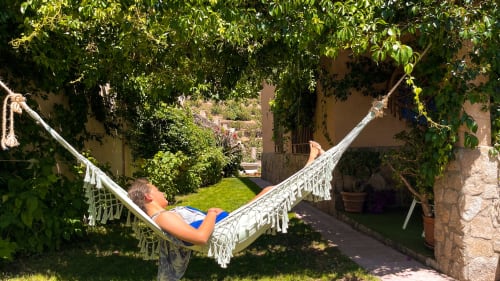 Huésped descansando en hamaca en Casa Rural Villa del Jerte, rodeado de exuberante vegetación y arquitectura rústica de piedra en El