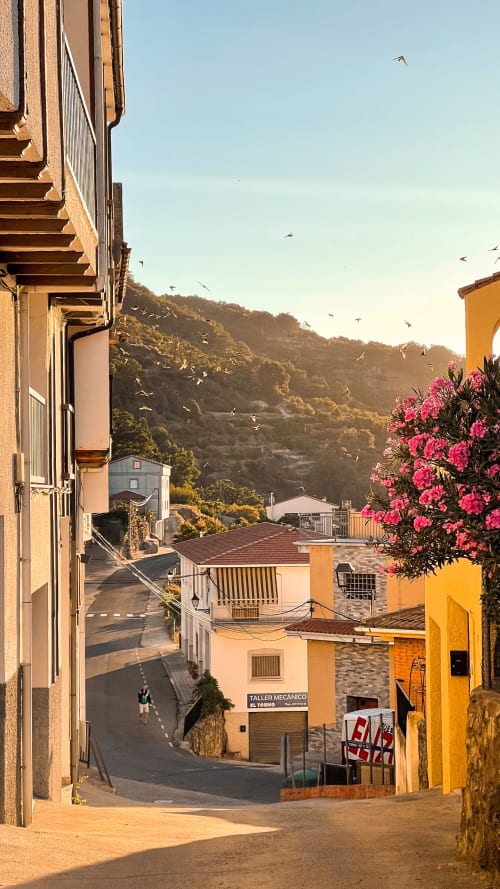 Charming village street in El Torno with colorful buildings, blooming flowers, and forested hills at Casa Rural Villa del