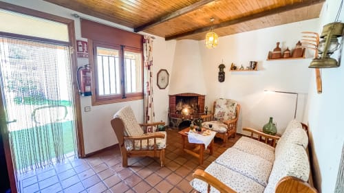 Acogedora sala de estar en Casa Rural Villa del Jerte con chimenea, vigas de madera, muebles tradicionales y suelos de barro