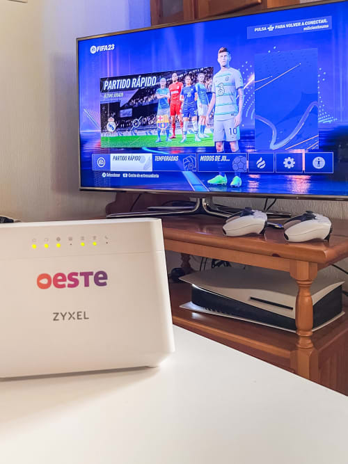 Sala de estar de Casa Rural Villa del Jerte con televisor mostrando FIFA 23, router y controles de videojuegos sobre escritorio de madera