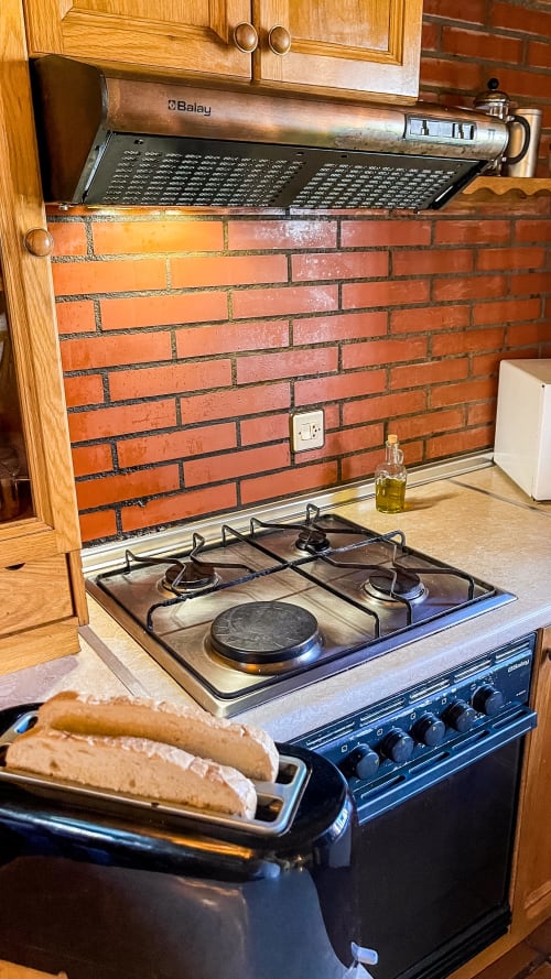 Estufa de cocina con encimera de gas, campana Balay y salpicadero de ladrillo en Casa Rural Villa del Jerte