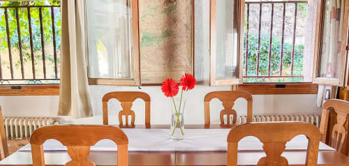 Comedor luminoso de Casa Rural Villa del Jerte con sillas de madera, flores rojas y vistas al jardín a través de grandes ventanales