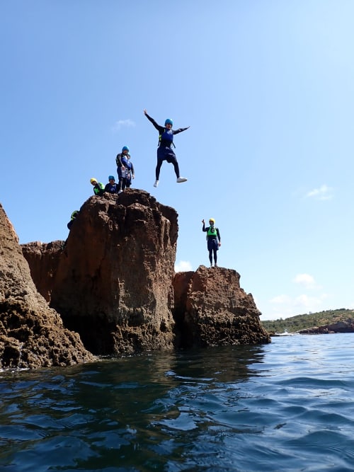Adventure seekers cliff jumping at Bordeira, Portugal coastal rocks with clear blue water and sky