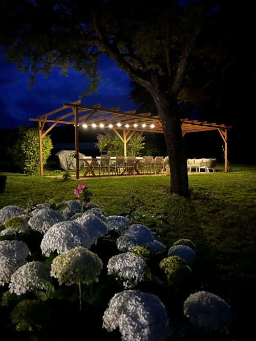 Illuminated wooden pergola with dining setup at Le Prieuré Du Preux, France, evening outdoor seating area