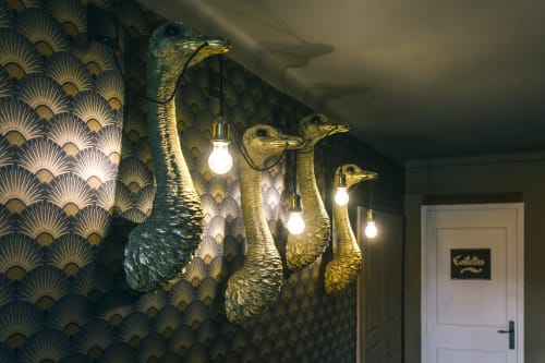 Appliques murales en or en forme de tête de paon avec lumières brillantes contre un papier peint à motifs au Prieuré Du Preux B&B