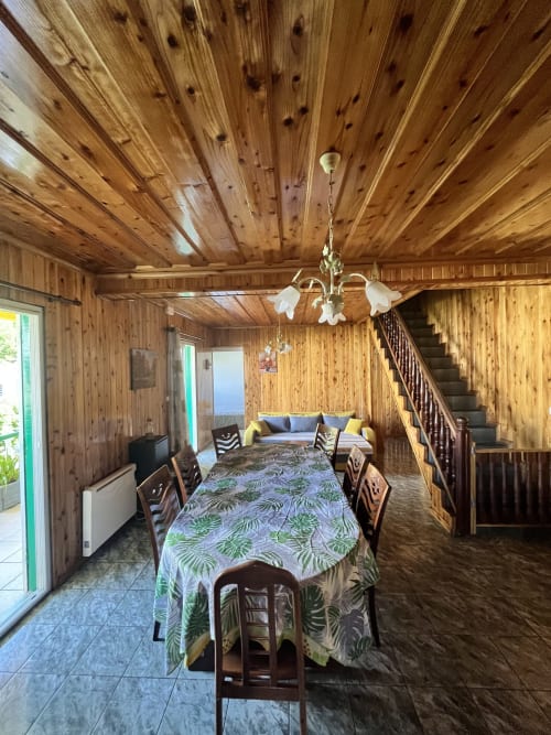 Salle à manger du lodge en bois à Au pied des Sources, Cilaos, avec table commune, lustre et escalier