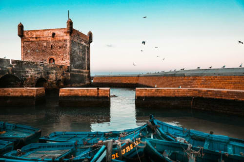 Historische haven met blauwe vissersboot en stenen versterkingstoren in Essaouira, poort aan de Marokkaanse kust