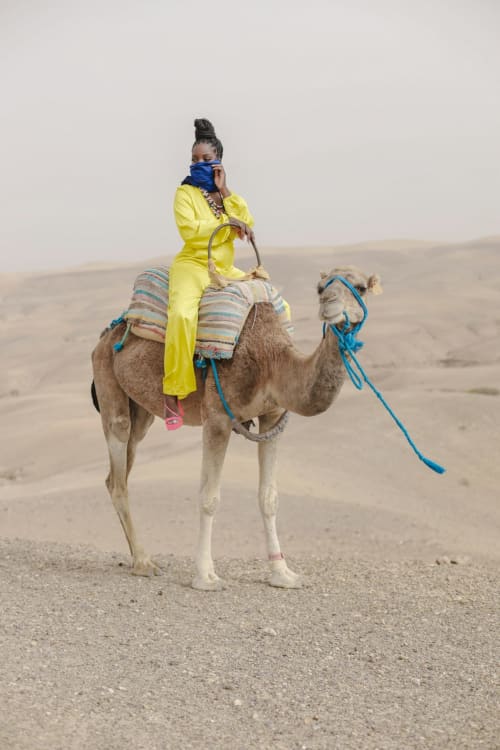 Vrouw in geel outfit rijdend op een kameel in de woestijn van Marrakesh nabij Riad Palau Marrakech