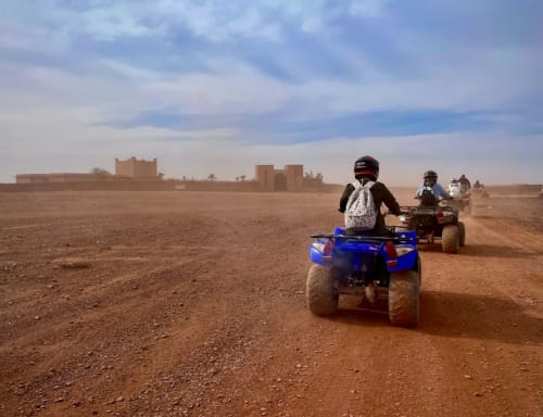 ATV riders on desert trail near Marrakech with kasbah ruins in background