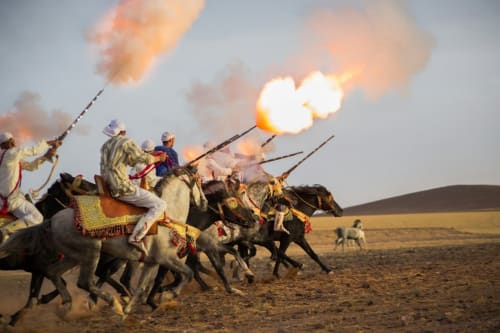 Traditional Moroccan cavalry performers on horseback with flaming torches in Marrakesh desert near Riad Palau