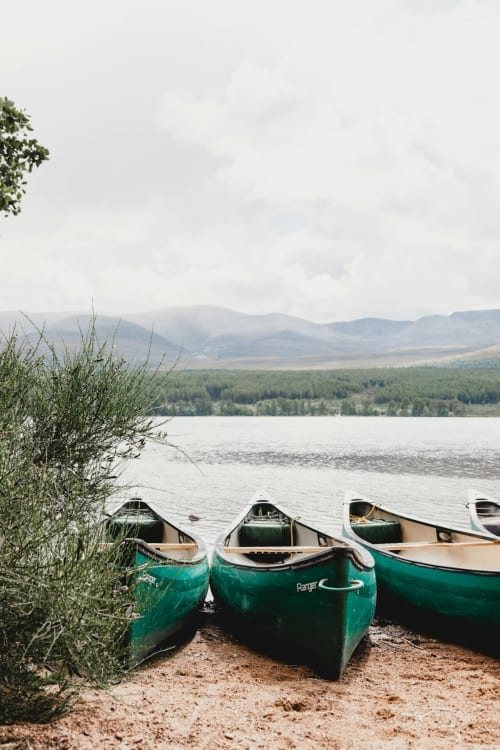 Green canoes beached on sandy shore with misty mountains and forested landscape beyond, Arrochoile accommodation near Glasgow