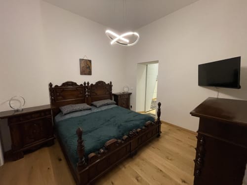 Camera da letto moderna nell'appartamento Saint Michel a Gorizia con letto in legno ornato, biancheria teal, mobili scuri, TV a schermo piatto e