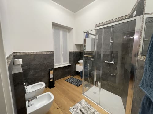 Bagno moderno dell'appartamento Saint Michel a Gorizia, con piastrelle scure, doccia in vetro, doppio lavabo e rivestimenti in legno