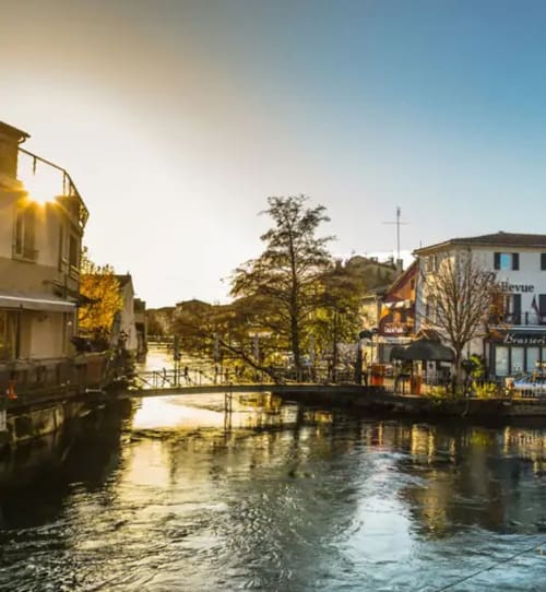 Charming waterfront view of Domaine des Lavarines B&B in Morières-lès-Avignon with stone buildings and trees along the canal