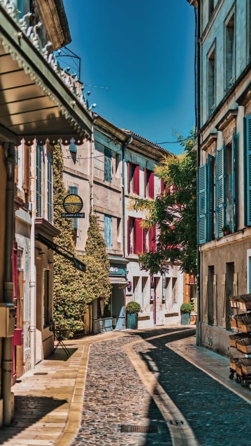 Charming narrow street in Morières-lès-Avignon with ivy-covered buildings, red shutters, and clear blue sky