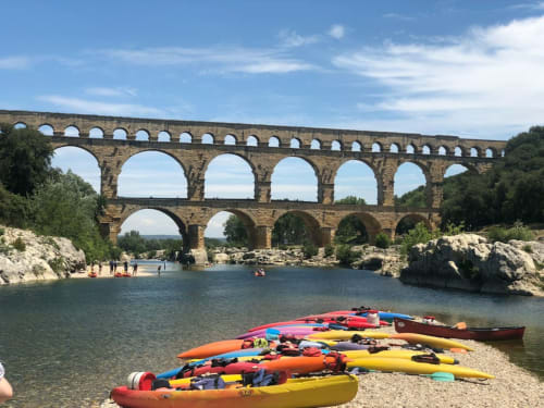 Colorful kayaks lined up on a beach near the ancient Pont du Gard aqueduct in Morières-lès-Avignon