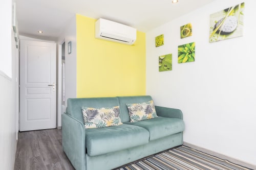 Bright studio with mint sofa, yellow accent wall, and plant artwork at Azur Studios Cannes