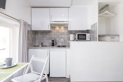 Compact kitchenette at Azur Studios Cannes with white cabinetry, patterned backtile, stovetop, microwave and dining area