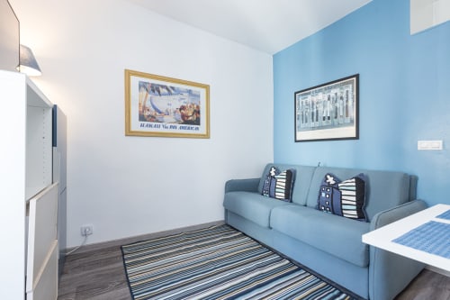 Superior Studio at Azur Studios Cannes with blue walls, sofa, striped rug, and vintage travel posters