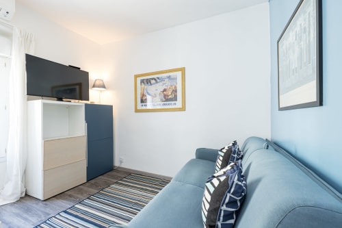 Modern studio apartment at Azur Studios Cannes with blue sofa, flat-screen TV, kitchenette, and city view décor