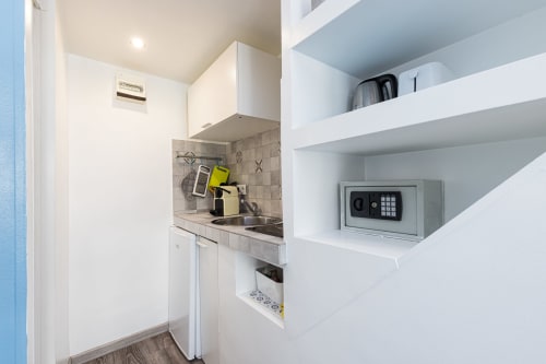 Compact kitchenette with white cabinets, stove, and built-in shelving with safe in Superior Studio at Azur Studios Cannes