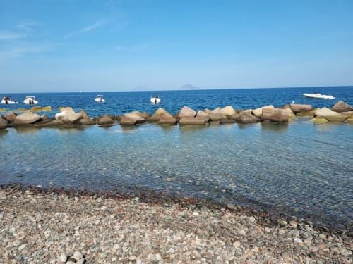 Rocky breakwater and moored boats at Miravilla Salina beach, Santa Marina Salina, Italy