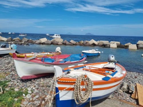Colorful fishing boats moored on pebble beach at Miravilla Salina, Santa Marina Salina, Italy with calm blue waters and rocky