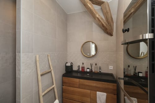 Moderne badkamer in het Moulin Renaudiots in Autun met houten wastafel, zwart werkblad, rond spiegelwand en beige tegels