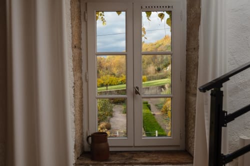 French doors open to autumn garden view at Moulin Renaudiots in Autun, with rustic pitcher and stone walls