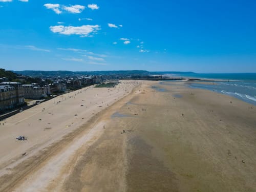 Vue aérienne de la plage de sable de Trouville-sur-Mer avec l'Hôtel Le Trouville à gauche et la mer bleue au-delà