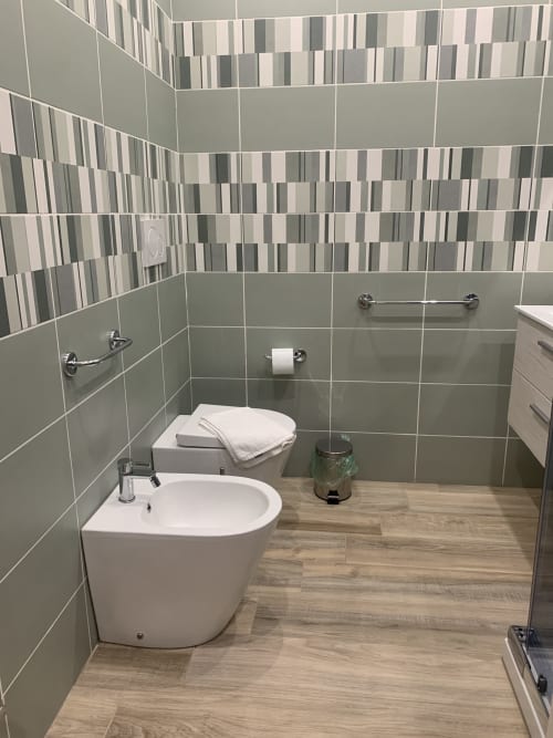 Modern bathroom at Maryam 23 guesthouse in Siracusa featuring gray striped tiles, white round toilet, and wood-effect