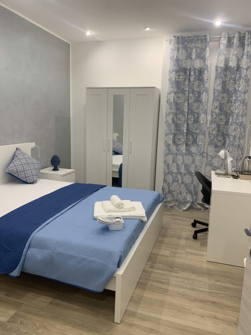 Modern blue bedroom at Maryam 23 B&B in Siracusa with white wardrobe, desk, and floral curtains