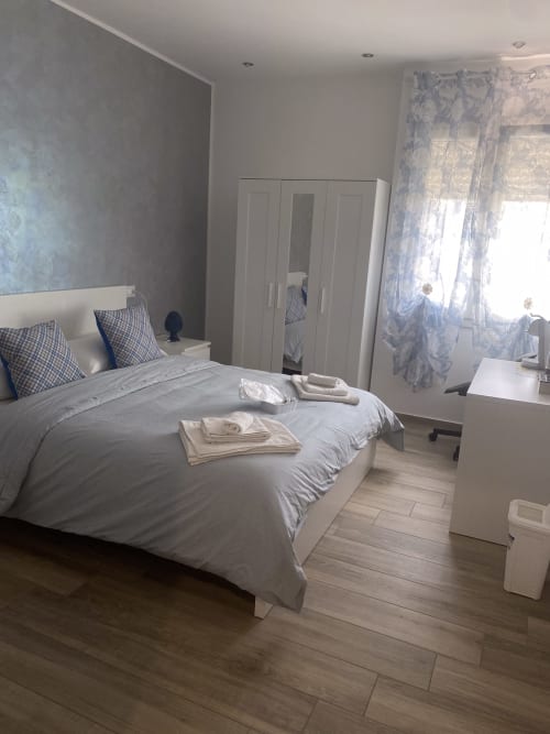 Modern bedroom at Maryam 23 B&B in Siracusa with white bed, mirrored wardrobe, and blue patterned curtains
