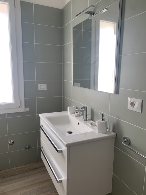 Modern bathroom in Maryam 23 B&B, Siracusa with white vanity, gray tile walls, and mirror with lighting