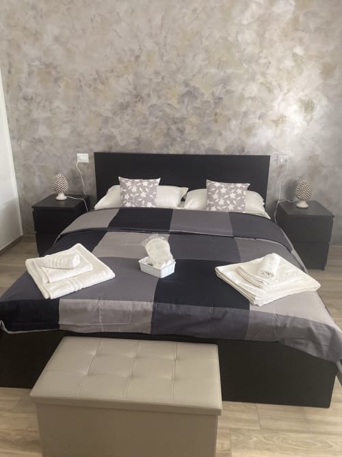 Modern black and white bedroom at Maryam 23 B&B in Siracusa with striped bedding, nightstands, and white bench