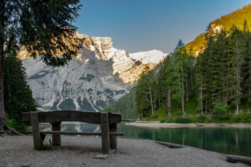 Panchina in legno con vista su lago alpino, montagne innevate e bosco vicino all'Hotel Le Clou, Arvier