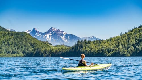 Person beim Kajakfahren auf einem Alpensee mit schneebedeckten Bergen und Wald in der Nähe von Arvier, Italien
