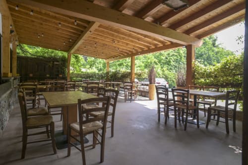 Area dining all'aperto coperta dell'Hotel Le Clou ad Arvier con tavoli in legno, sedie in paglia e vista sugli alberi