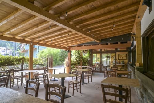 Area ristorazione con pergolato in legno all'Hotel Le Clou di Arvier, sedie rustiche e tavoli con vista sui giardini