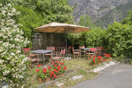 Area dining esterna dell'Hotel Le Clou ad Arvier con ombrelloni, sedie rosse e piante fiorite