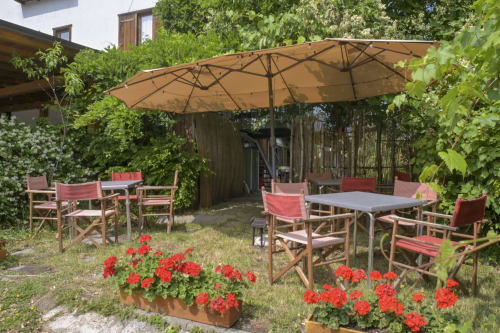 Soleggiata terrazza dell'Hotel Le Clou con ombrellone, sedie in legno e gerani rossi ad Arvier