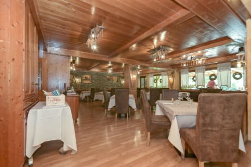 Elegante sala da pranzo dell'Hotel Le Clou ad Arvier con travi in legno, tovaglie bianche e ghirlande festose