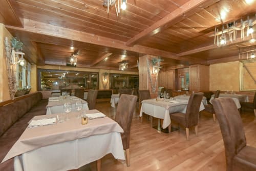 Elegante sala da pranzo dell'Hotel Le Clou ad Arvier con travi in legno, tovaglie bianche e sedie imbottite