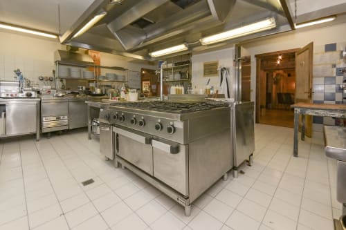 Cucina professionale dell'Hotel Le Clou ad Arvier con fornello, forni e superfici di preparazione in acciaio inossidabile